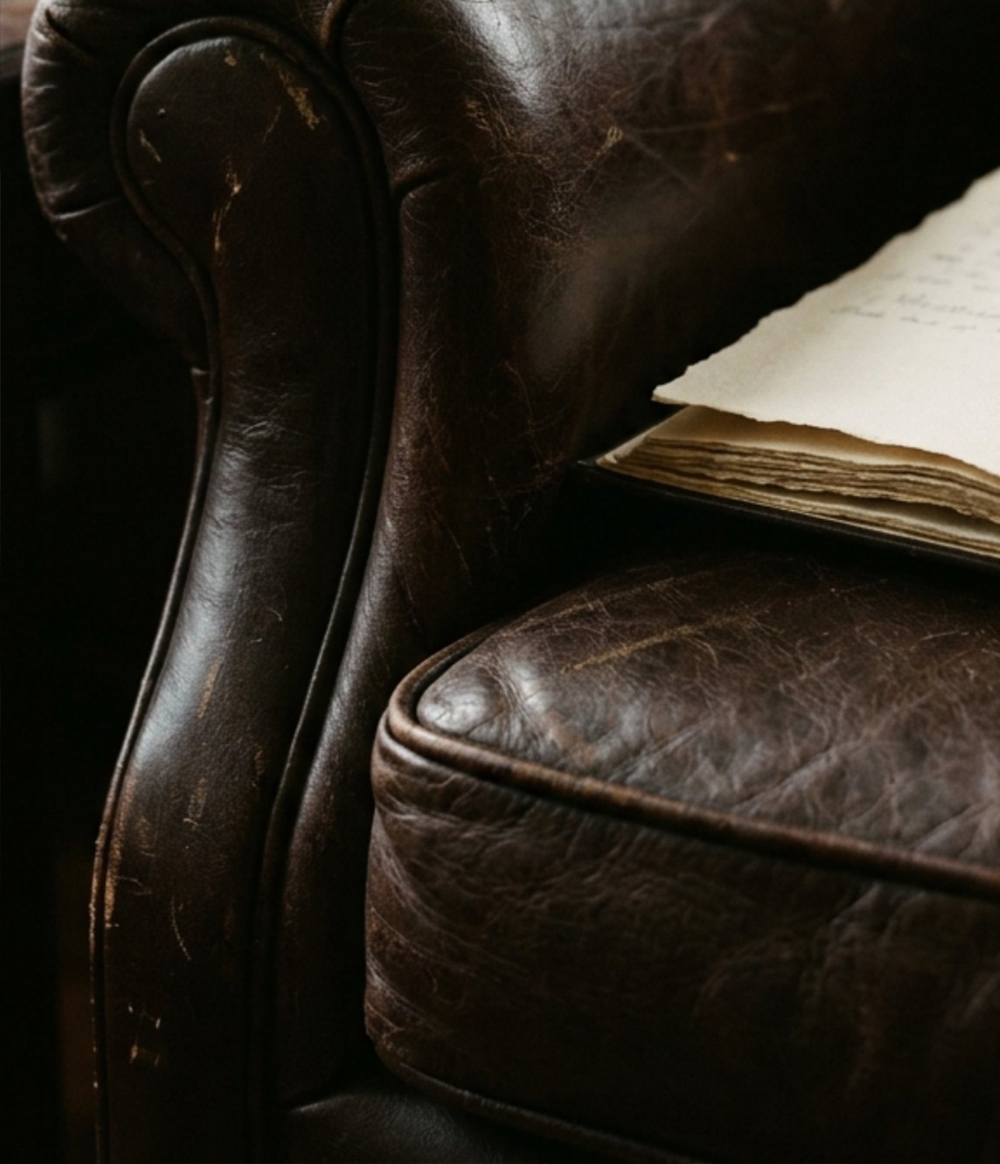 The worn leather arm of a consulting-room chair, an open notebook resting beside it